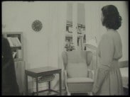 En kvinna i en lägenhet, en fåtölj och ett fönster mitt i bild.