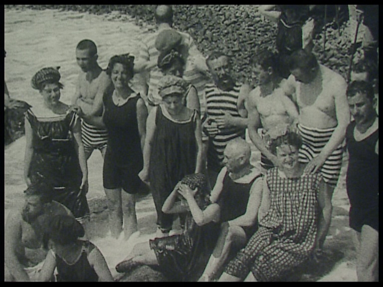 Ett myller av badande damer och herrar i tidsenliga baddräkter visar upp sig för kameran på stranden vid Mölle.