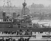 Helbild av flaggsmyckad hamn med ett krigsfartyg, paraderande trupper etc.