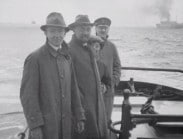 Fyra personer i en båt till havs, fartyg i bakgrunden.