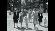 Ett tiotal kvinnor och barn utomhus på sommaren, en del håller varandra i handen. Tallar i bakgrunden.