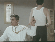 En läkare med stetoskop lyssnar på lungorna på en man i vitt linne med ryggen mot kameran, syntavla i bakgrunden.