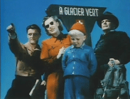 Tre vuxna och ett barn i moderiktiga kläder under en skylt med texten À glacier vert.