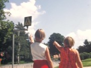 Två sommarklädda barn filmade bakifrån pekar upp mot en vägskylt för övergångsställe.
