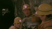 Tre gruvarbetare med gula hjälmar med pannlampor.