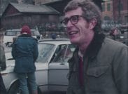 En leende Bo Widerberg under inspelningen av Mannen på taket, polisbilar och människor i bakgrunden.