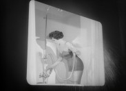 En kvinna iklädd baddräkt ståendes i ett badkar sprutar vatten ur duschmunstycket utanför karet.