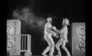 Två män i vita scenkostymer boxas, stora tvålpaket i bakgrunden på respektive sida.