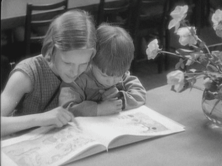 En flicka tillsammans med en yngre pojken som läser tillsammans i en bok.