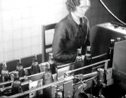 En kvinna på en fabrik vid ett löpande band med glasflaskor.