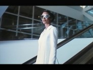 En kvinna i vit klänning och med solglasögon åker rulltrappa.