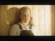 En ung flicka i snickarbyxor mot en träpanel.