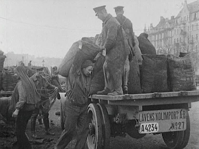 Några män lastar säckar med kol på en lastbil av äldre modell med öppet flak.