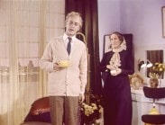 Jarl Kulle i salong med en gul kaffekopp, kvinna klädd i lila i bakgrunden.