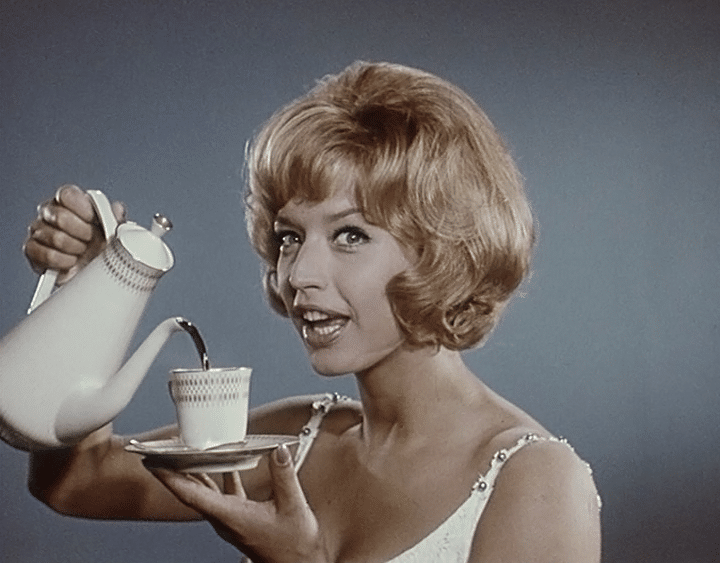 Lill-Babs häller upp kaffe ur en kanna i en kopp på fat.