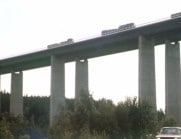 Jättelik betongbro fotad ur grodperspektiv, lastbilar med släp kör på den.