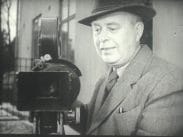 Fotografen Gustaf Boge i hatt bredvid en filmkamera.