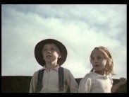 En pojke i tioårsåldern med hatt och hängslen bredvid en flicka i samma ålder, himmel i bakgrunden.