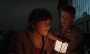 Två unga pojkar inomhus i svag belysning med en ljuskälla i förgrunden.