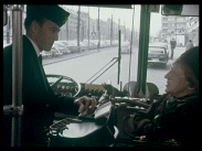Äldre kvinna i hatt löser biljett av busschaufför i stadstrafik.