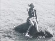 En ung kvinna sitter på en klipphäll i havet med fötterna i vattnet.