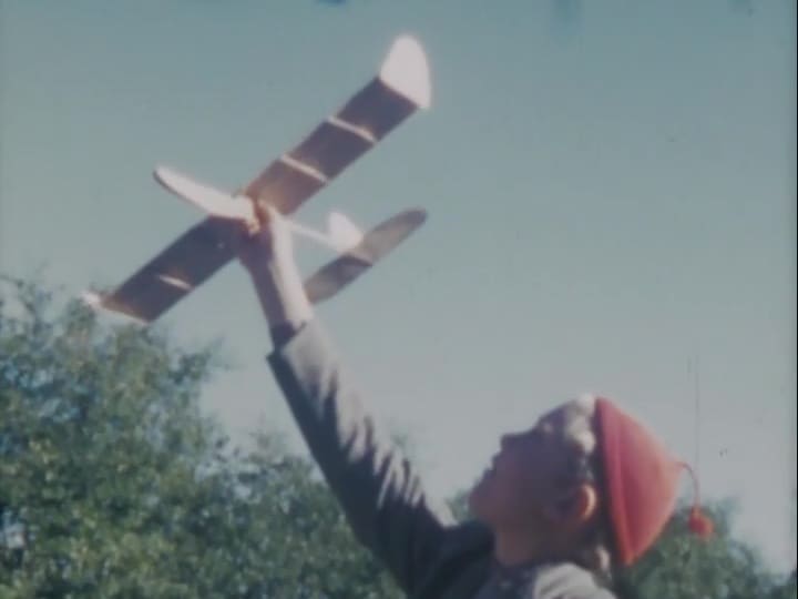 Pojke i röd toppluva leker med egentillverkat modellflygplan.