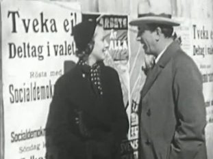 Ung kvinna och medelålders man framför affischvägg med socialdemokratiska valaffischer.