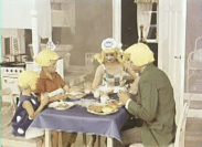 En familj runt frukostbord, alla bär gula peruker.