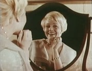 Christina Schollin ler och tittar sig i en spegel.