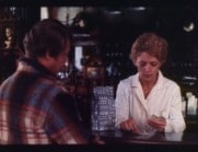 En kvinnlig servitris räknar upp kontanter på en bardisk, väntande manlig kund med ryggen mot kameran.