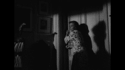 Kvinna i mörker vid dörr på glänt.