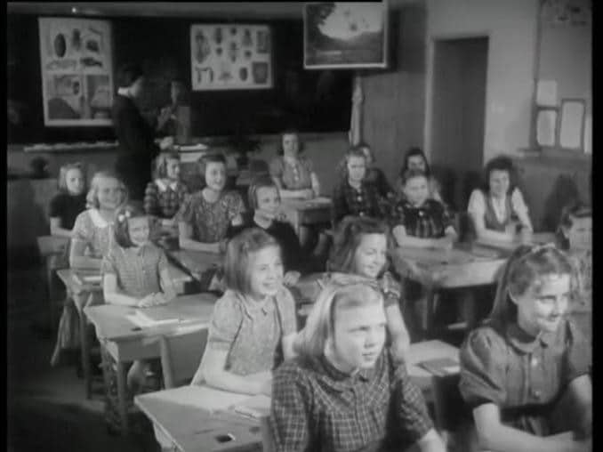 Barn sitter vid skolbänkar i ett klassrum.