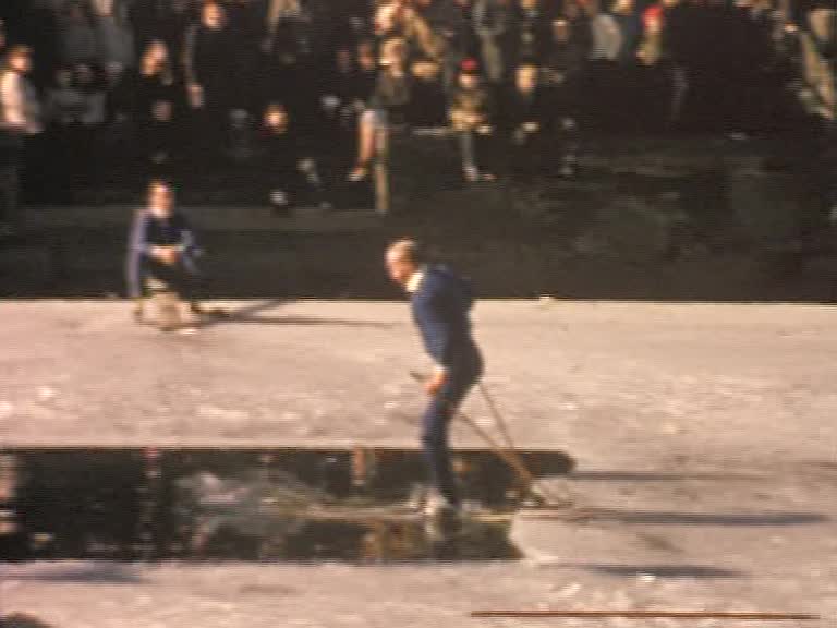 En man på längdskidor åker ner i en isvak, publik i bakgrunden.