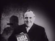 En leende man håller upp ett häfte med texten "Sparbankernas kassabok".