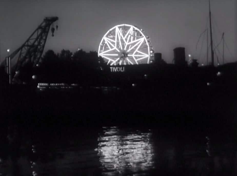 Mörk bild med ett upplyst pariserhjul och texten "TIVOLI" under, siluetten av en lyftkran till vänster.