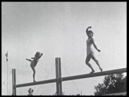 Ett par kvinnor utför gymnastiska balansövningar på en bom utomhus.