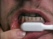 Närbild av munnen på en man med mustasch som borstar tänderna med en vit tandborste.