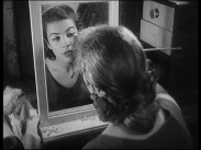 Adrienne Lombard sminkar sig framför en spegel filmad bakifrån.