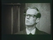 Närbild av en man med svarta bredbågade glasögon.