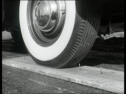 Närbild av ett bildäck med vit rand som rullar över en planka med uppåtstående spikar.
