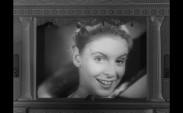 En leende kvinna tittar rakt in i kameran, teaterkuliss runtom.
