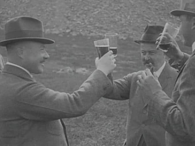Tre män i kostym och hatt skålar med varandra utomhus.