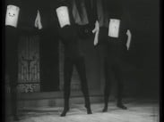 Tre svartklädda dansare med masker över huvudena bredvid varandra på en scen.