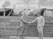 Två soldater med olika slags uniformer skakar hand, i bakgrunden en skylt som lyder: CAMP FRANCO-AMERICAIN.