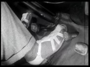 Närbild av en bilförares fötter i sandaler vid pedalerna.