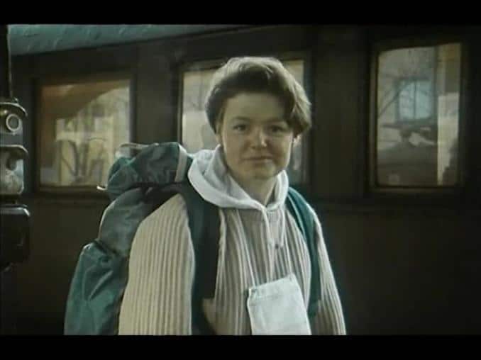 En ung kvinna med ryggsäck framför ett tåg.