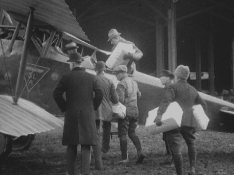 Stillbild från filmen Veckorevy 1920-03-01 som visar flera män som lastar ett flygplan med att antal paket.