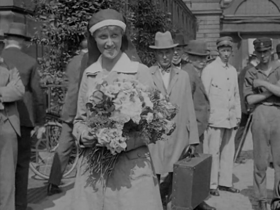 Elsa Brändström med blommor i famnen, människor i bakgrunden.