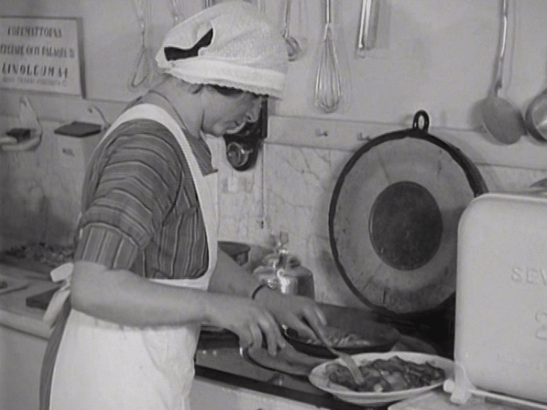 En kvinna klädd i arbetskläder lägger upp mat på ett fat.