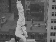 Vitklädd fasadklättrare står på huvudet på tak.